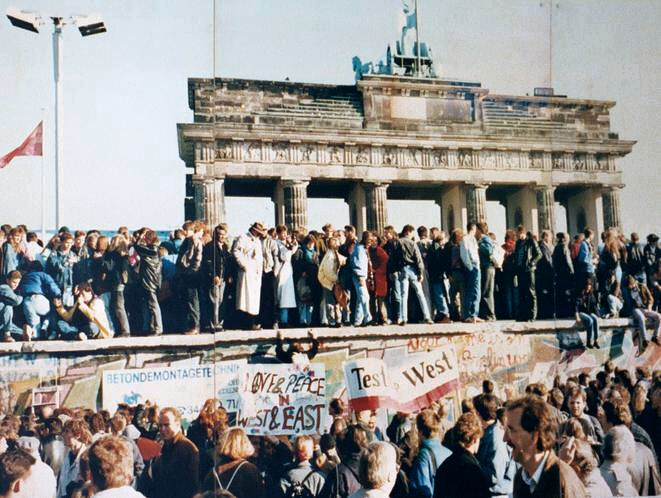 East and West Germans standing on the Berlin Wall near the Brandenburg Gate in 1989